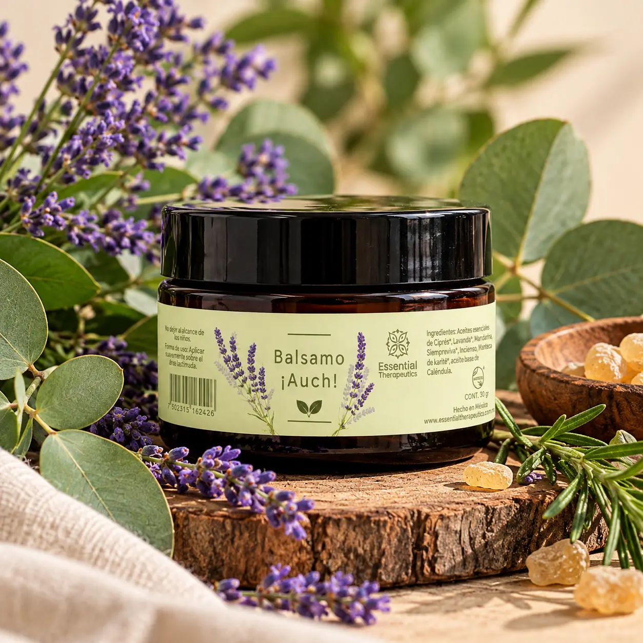 Bálsamo ¡Auch! de Essential Therapeutics de 30 g, rodeado de lavanda y hojas verdes sobre una base de madera.